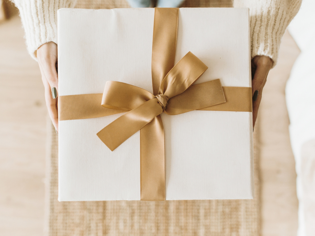 A person holds a beautifully wrapped white gift box with a golden ribbon, creating a warm and inviting feel. This image represents the excitement of receiving something special, just like our How To Print Free Printable Games guide, helping you easily enjoy fun, screen-free activities!
