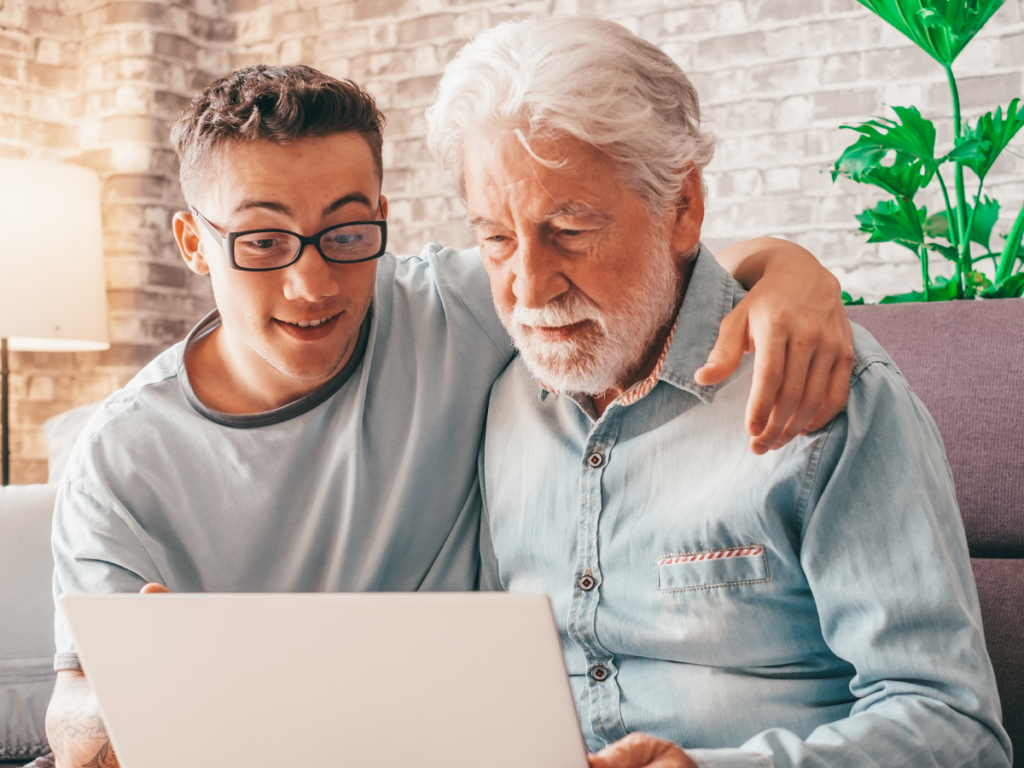 A young man and his grandfather sit together on a couch, smiling as they look at a laptop screen. This heartwarming moment highlights how Printable Games can bridge generations, bringing family members closer and creating meaningful connections through shared screen-free fun.