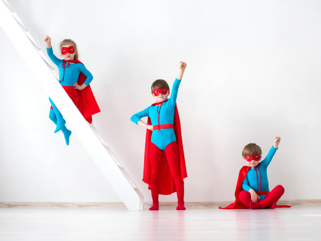 Three children in colorful superhero costumes striking fun poses, representing imaginative play and the power of screen-free fun using printable games and face-to-face interaction.